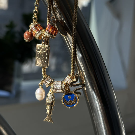 Medusa's Alchemy and Saltwater Spell charm necklaces hanging in golden light